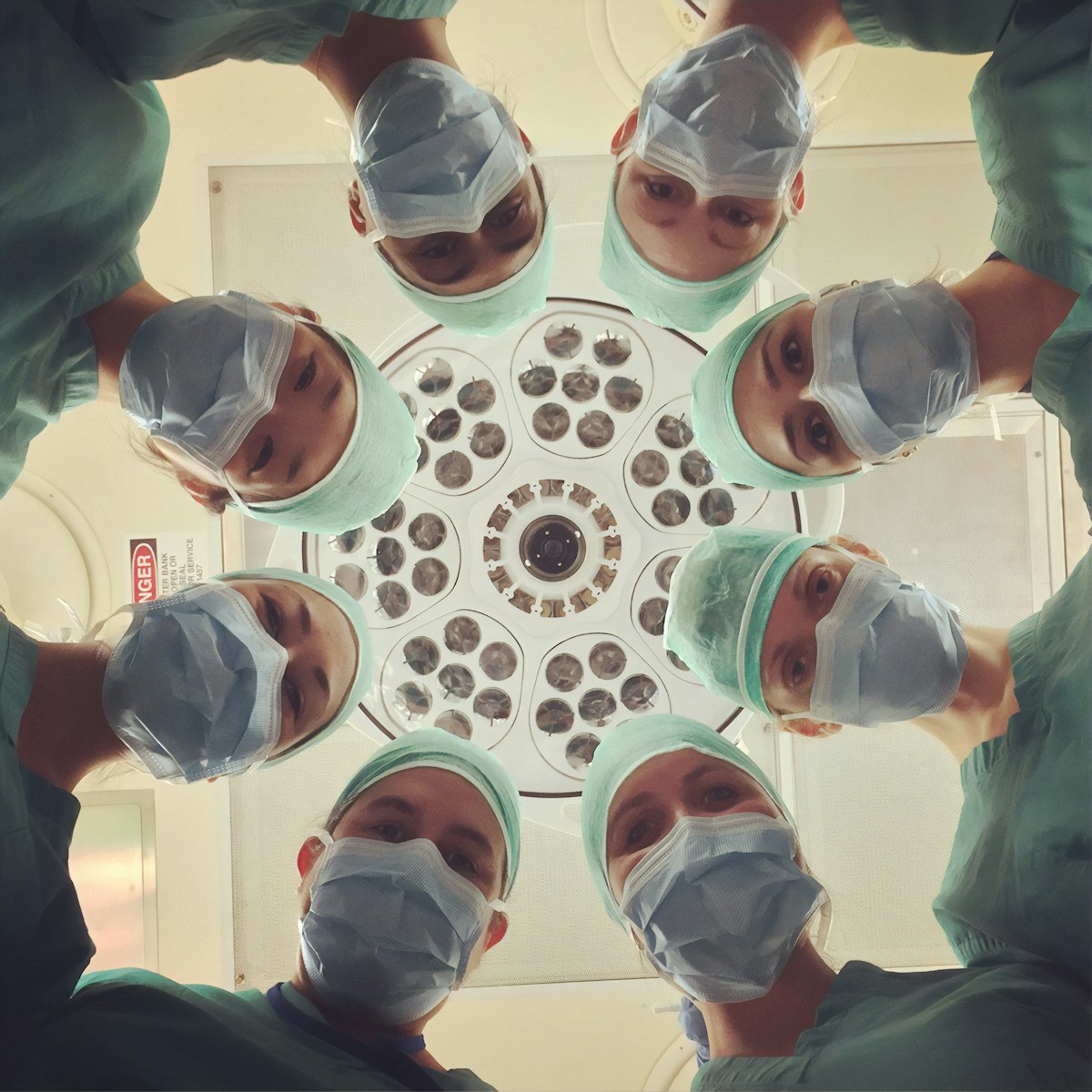A circle of hospital staff in scrubs looking up at the camera under an operating light